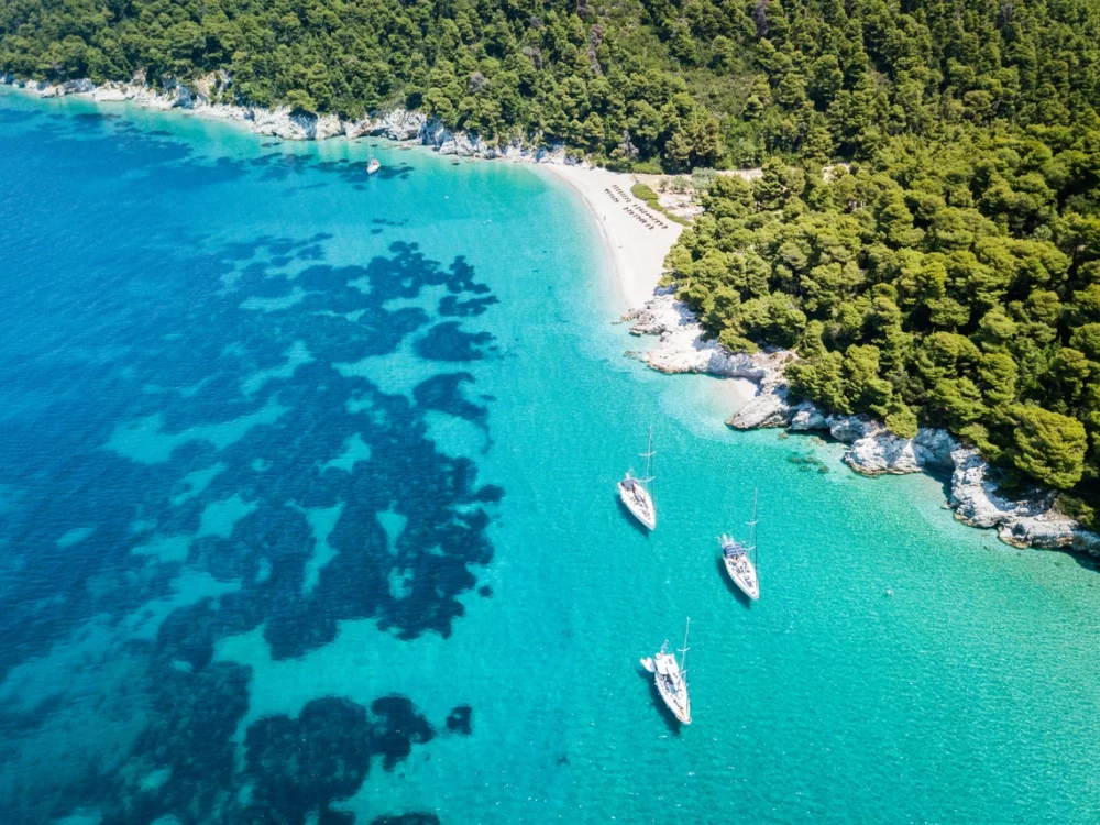 Aerial view of sailboats anchored in calm aqua water near Skopelos Island.