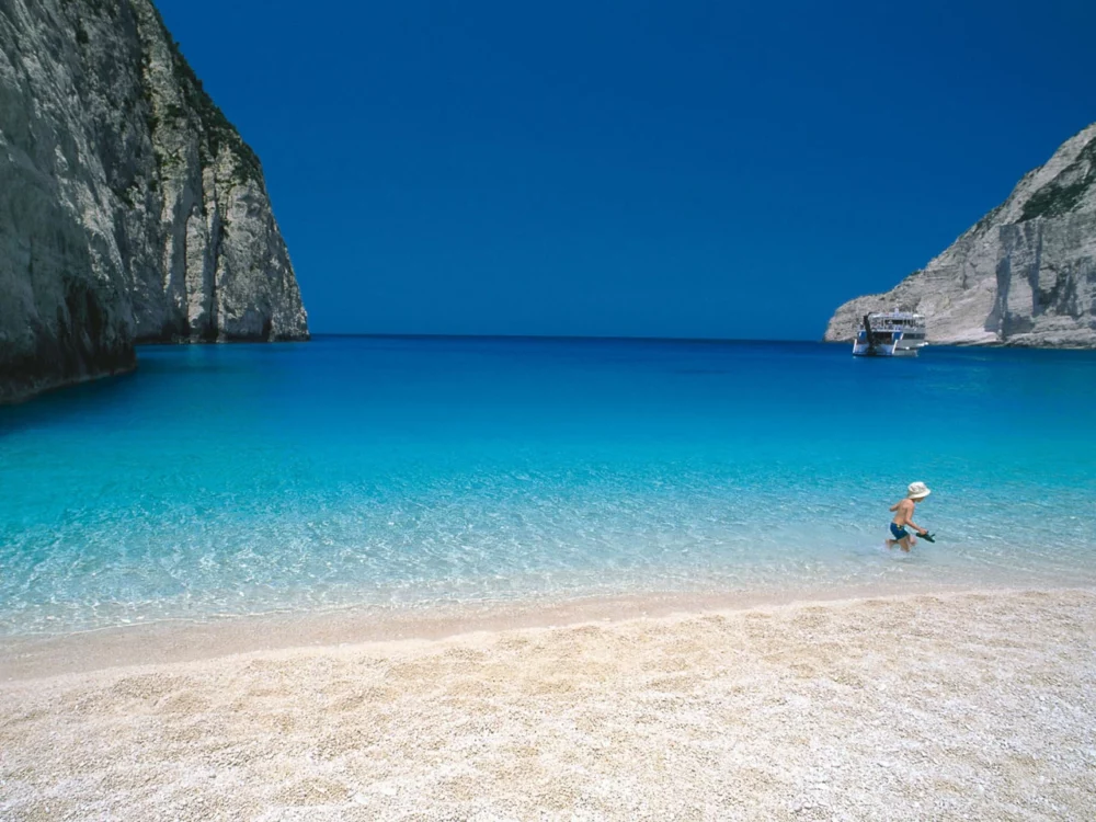 Zakynthos Beach: Crystal-clear aqua water, soft golden sand, a child playing in the water – a sensory paradise by the sea.