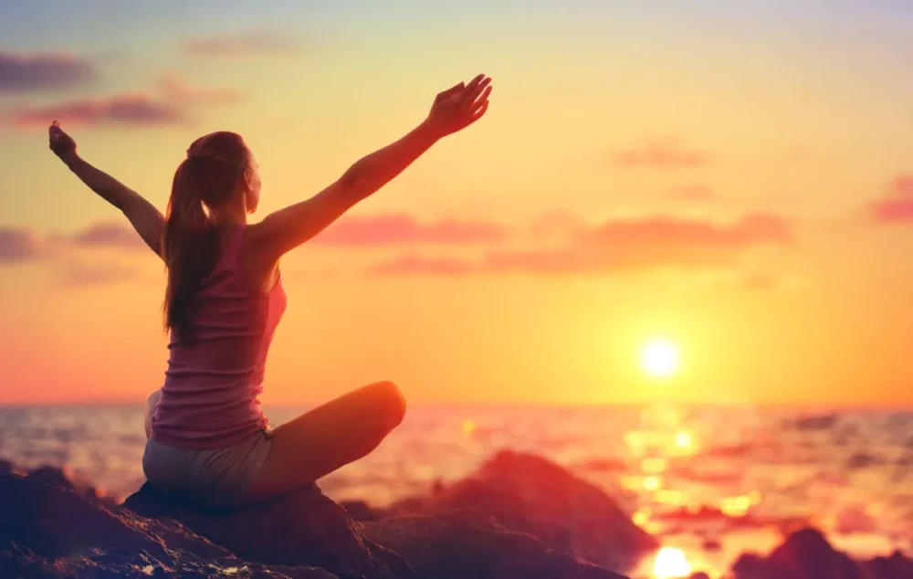 A woman siting in a lotus position enjoying the sunrise. Reflecting a Greece wellness yacht charter