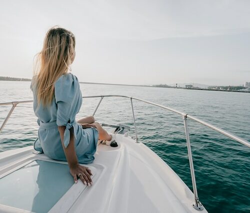 a woman in a dress sitting on the bow of a yacht
