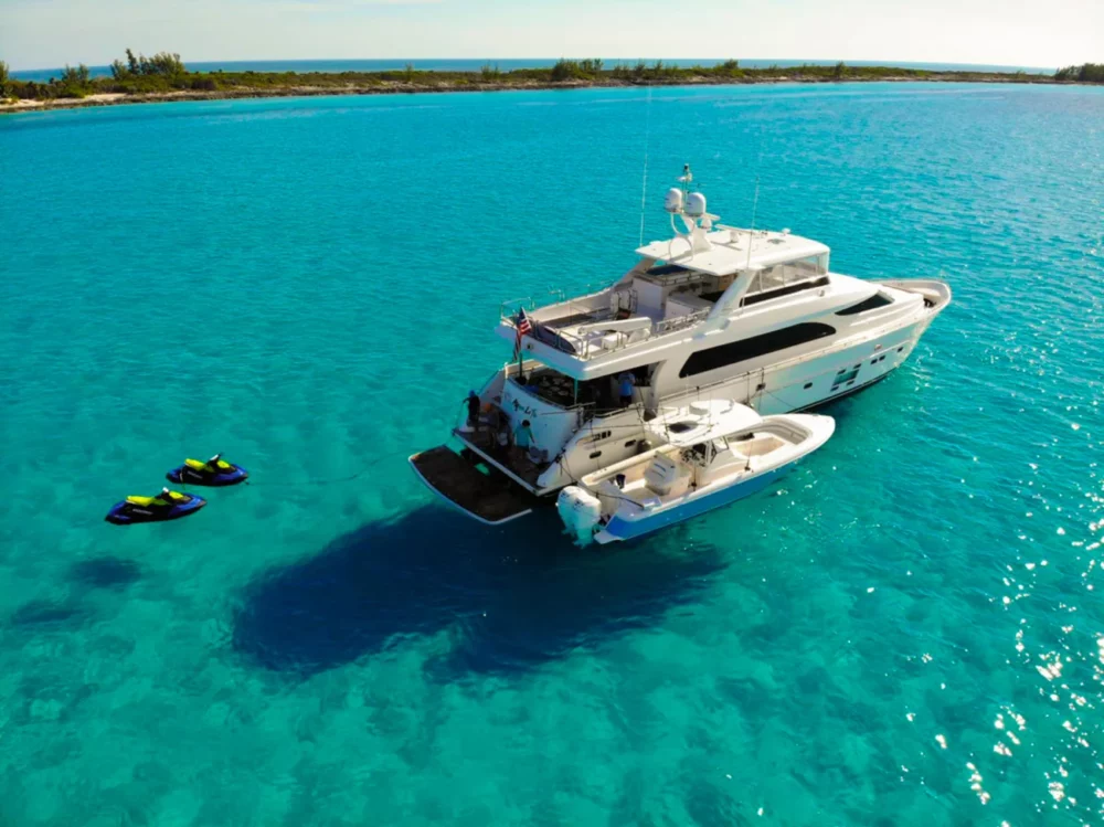Aerial view of the AQUA LIFE motor yacht anchored in the crystal-clear turquoise waters of the Caribbean, with jet skis floating nearby and a scenic island in the background, showcasing a premier Caribbean yacht charter experience.