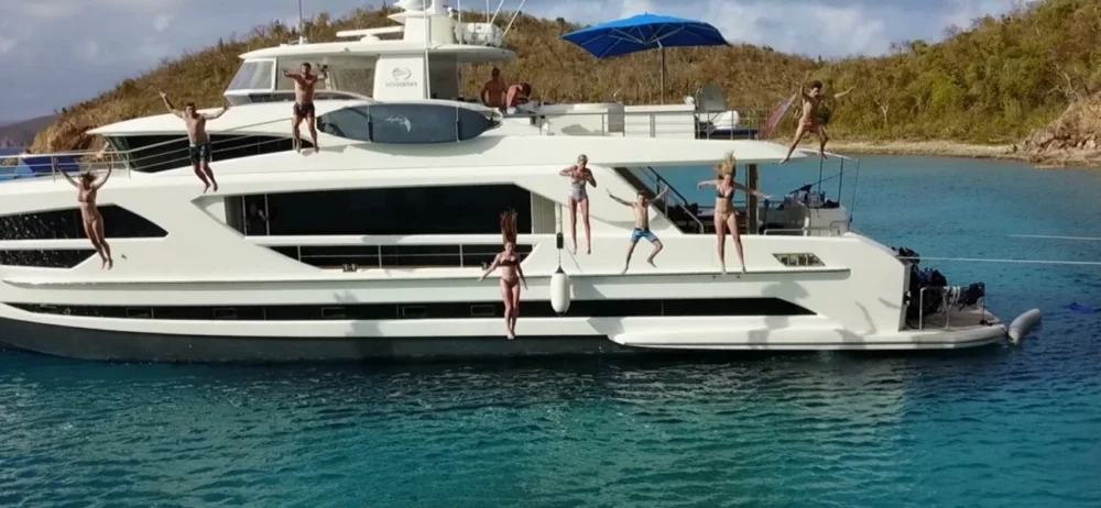 A group of people joyfully jumped off the luxurious ANGELEYES motor yacht into the clear blue waters of the Caribbean. The yacht is anchored near a serene island, illustrating an ideal scenario for those looking to rent a yacht in the Caribbean.
