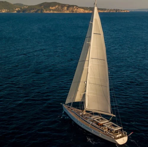 The SAVARONA sailing yacht charter is cruising through Caribbean waters near a coastal port, embodying the luxury and freedom of a boat charter in the Caribbean.