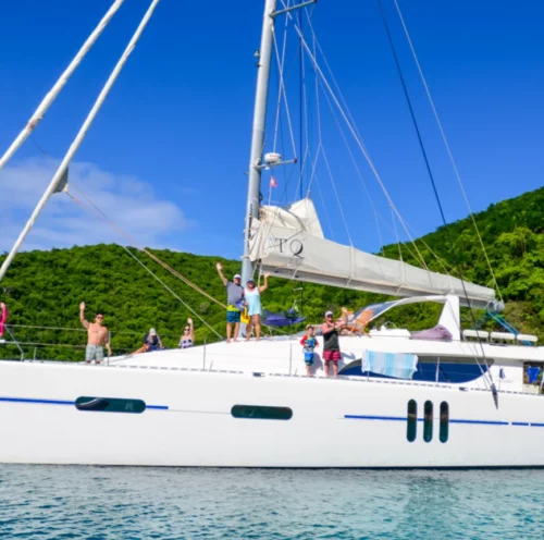 Families enjoying a day on the yacht Tranquility during their charter vacation in BVI waters, anchored near a lush green hillside under a clear blue sky.