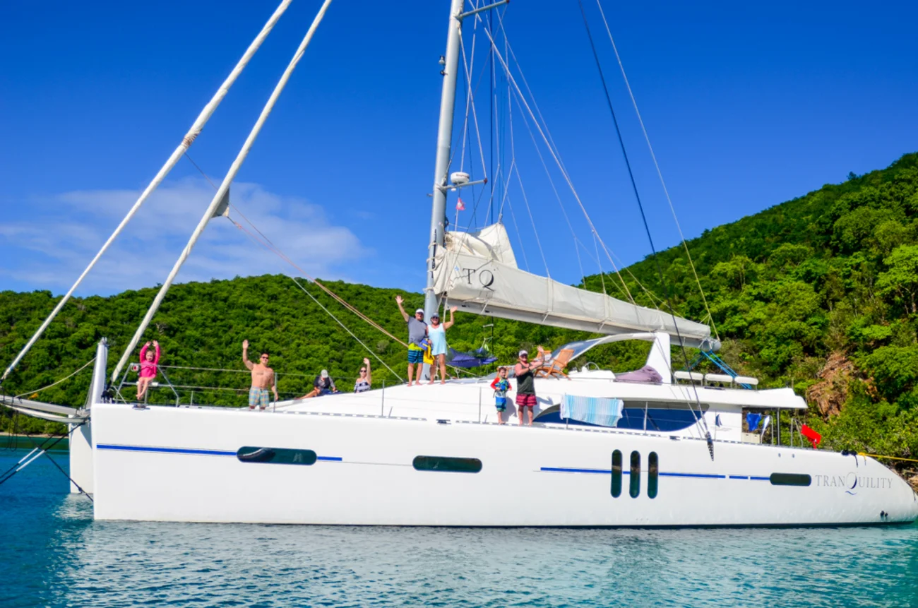 Families enjoying a day on the yacht Tranquility during their charter vacation in BVI waters, anchored near a lush green hillside under a clear blue sky.
