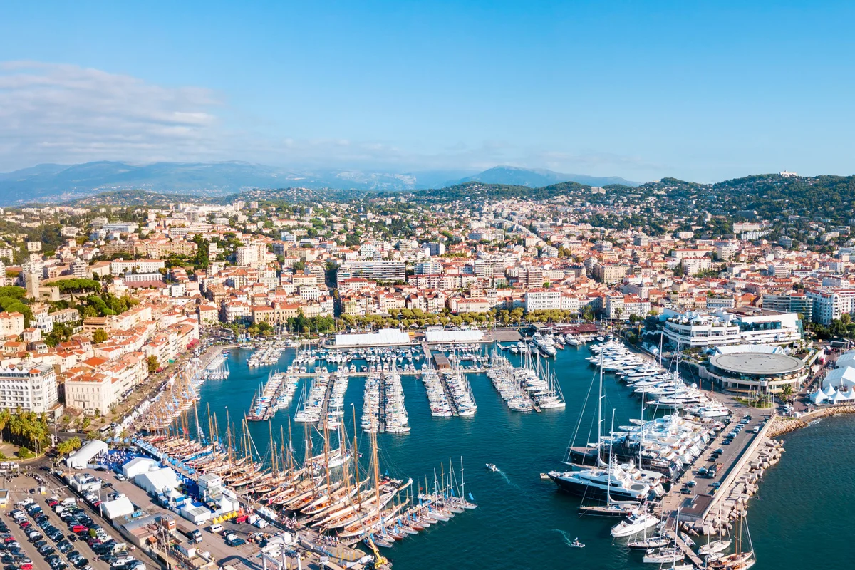 A picturesque view of the Cannes harbor filled with yachts, set against the backdrop of the city and hills.