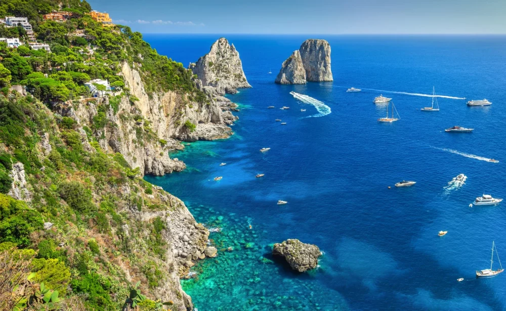 View of the dramatic cliffs and clear blue waters of Capri, Italy, a perfect destination for private yacht vacations, featuring luxury yachts and stunning landscapes.