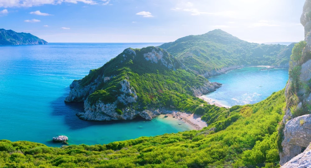 Lush green hills meet the sparkling Ionian Sea along the coast of Corfu Island, Greece. 