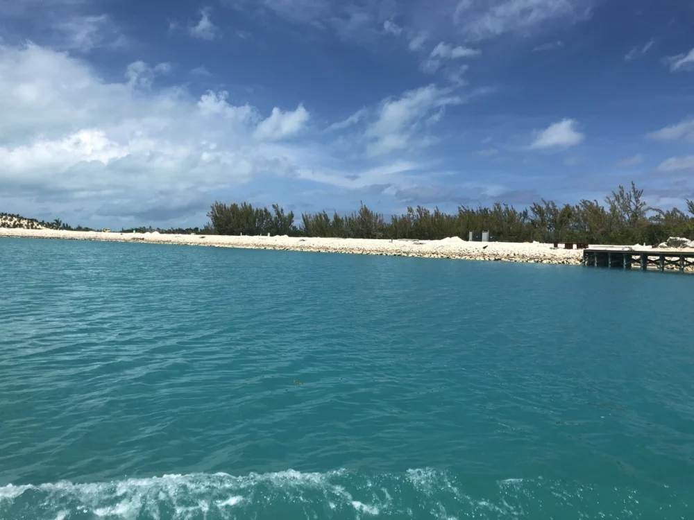 Scenic view of Exuma Bay with clear turquoise waters and a sandy shoreline, perfect for all-inclusive yacht charters, under a partly cloudy sky.