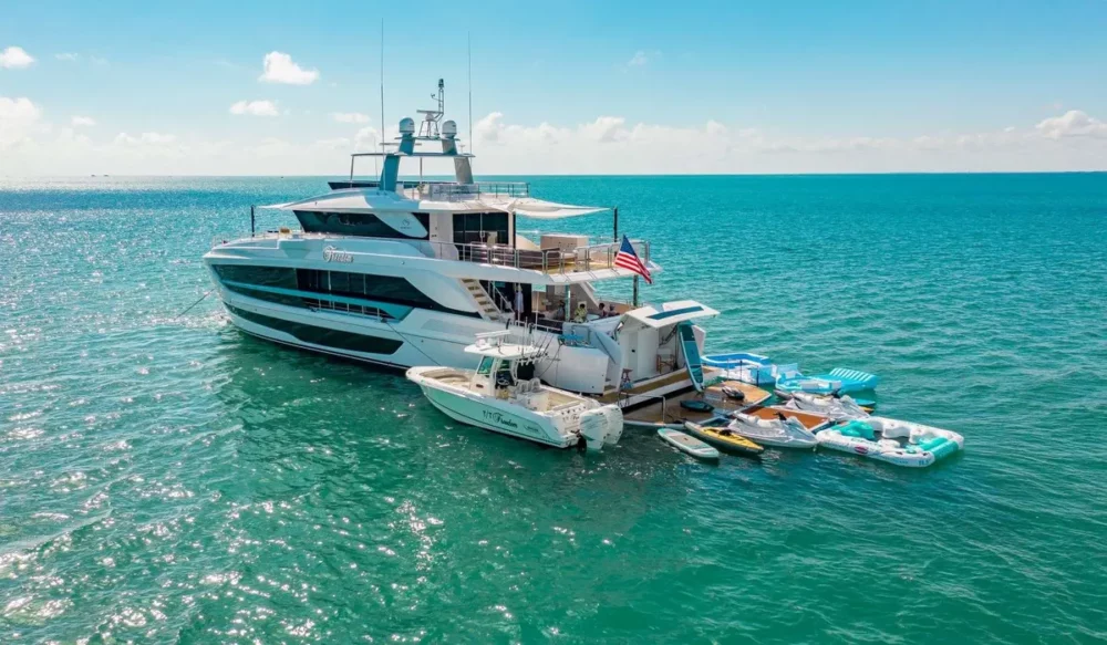 The FREEDOM motor yacht anchored in clear blue waters, surrounded by various water sports equipment and a smaller boat, offering a luxurious private yacht cruise experience.