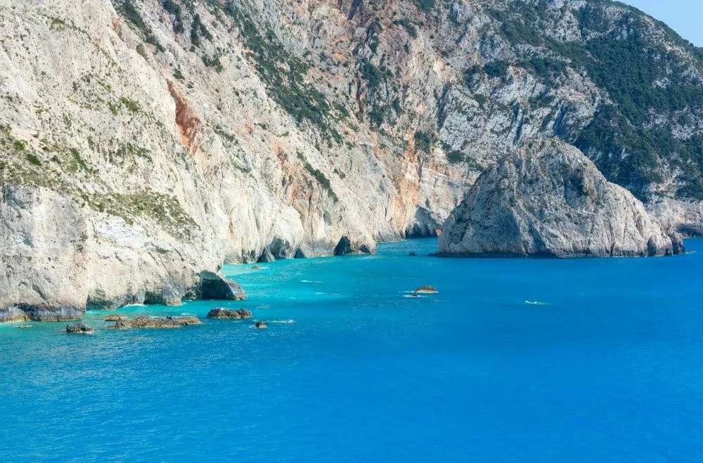 Greece coastline with rocky cliffs and in the blue waters of the Mediterranean.
