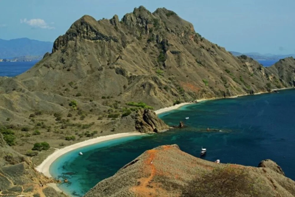 A panoramic view of Komodo Island in Indonesia, showcasing rugged hills and clear blue waters.