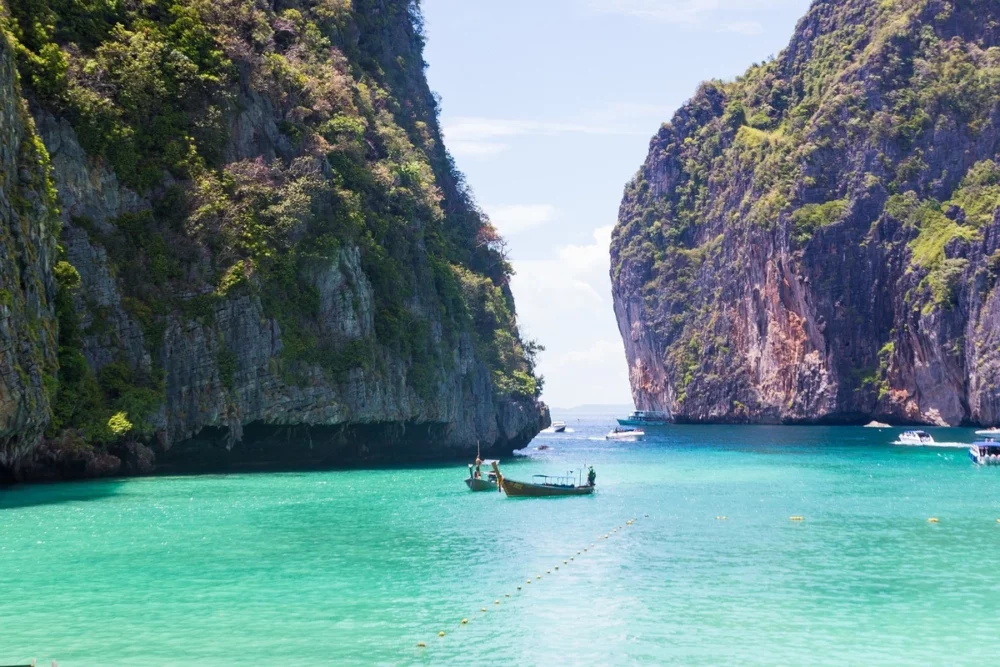 Scenic view of Maya Bay, Thailand, with turquoise waters, lush green cliffs, and boats floating in the bay.