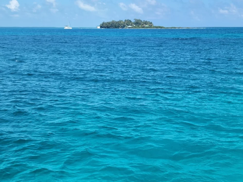 View of the turquoise waters around San Andres Island with a yacht in the distance and a small island on the horizon.