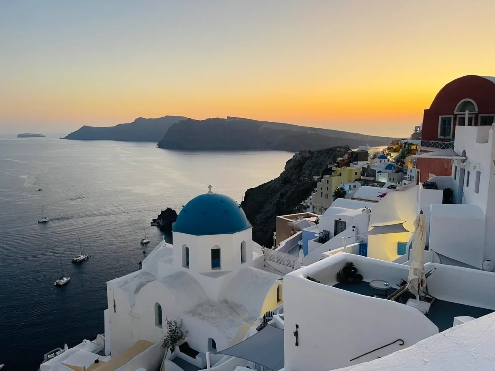  A stunning sunset view of Santorini, Greece, featuring white-washed buildings with blue domes overlooking the calm sea. 
