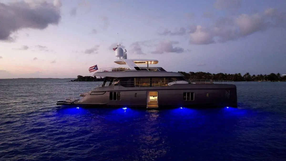 Luxury power catamaran Nauti Nickel anchored at dusk, illuminated by vibrant blue underwater lights,