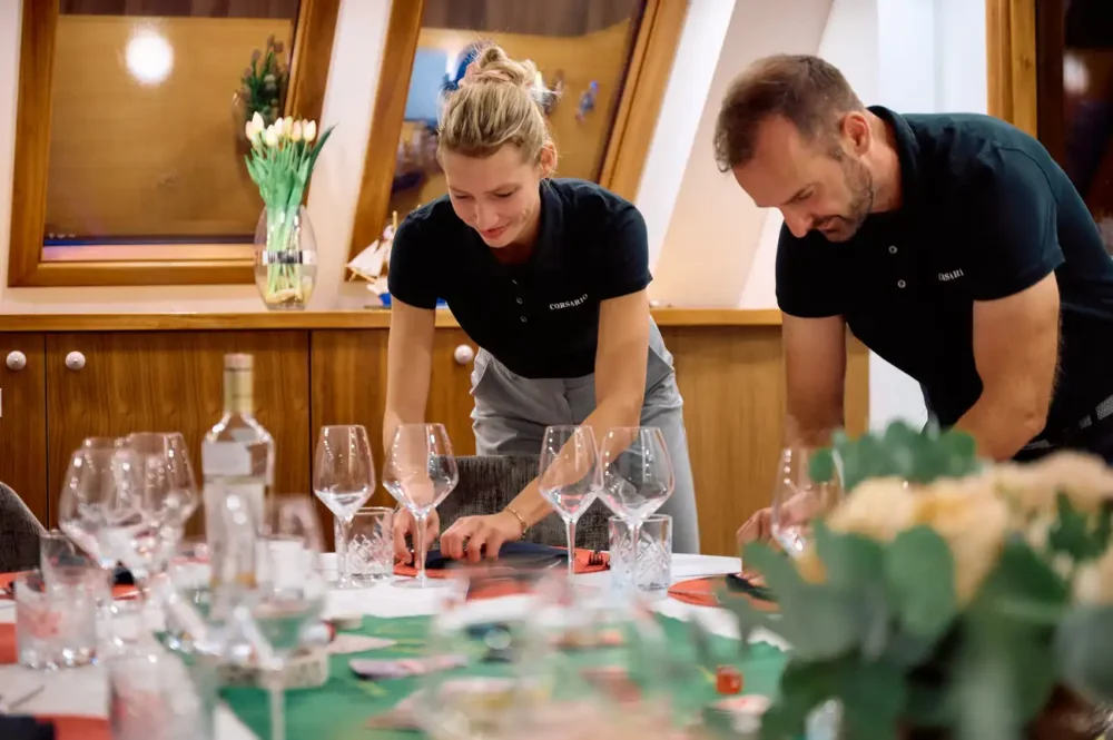 Corsario's stewardess and maitre d' completing the tablesetting for a gourmet charter